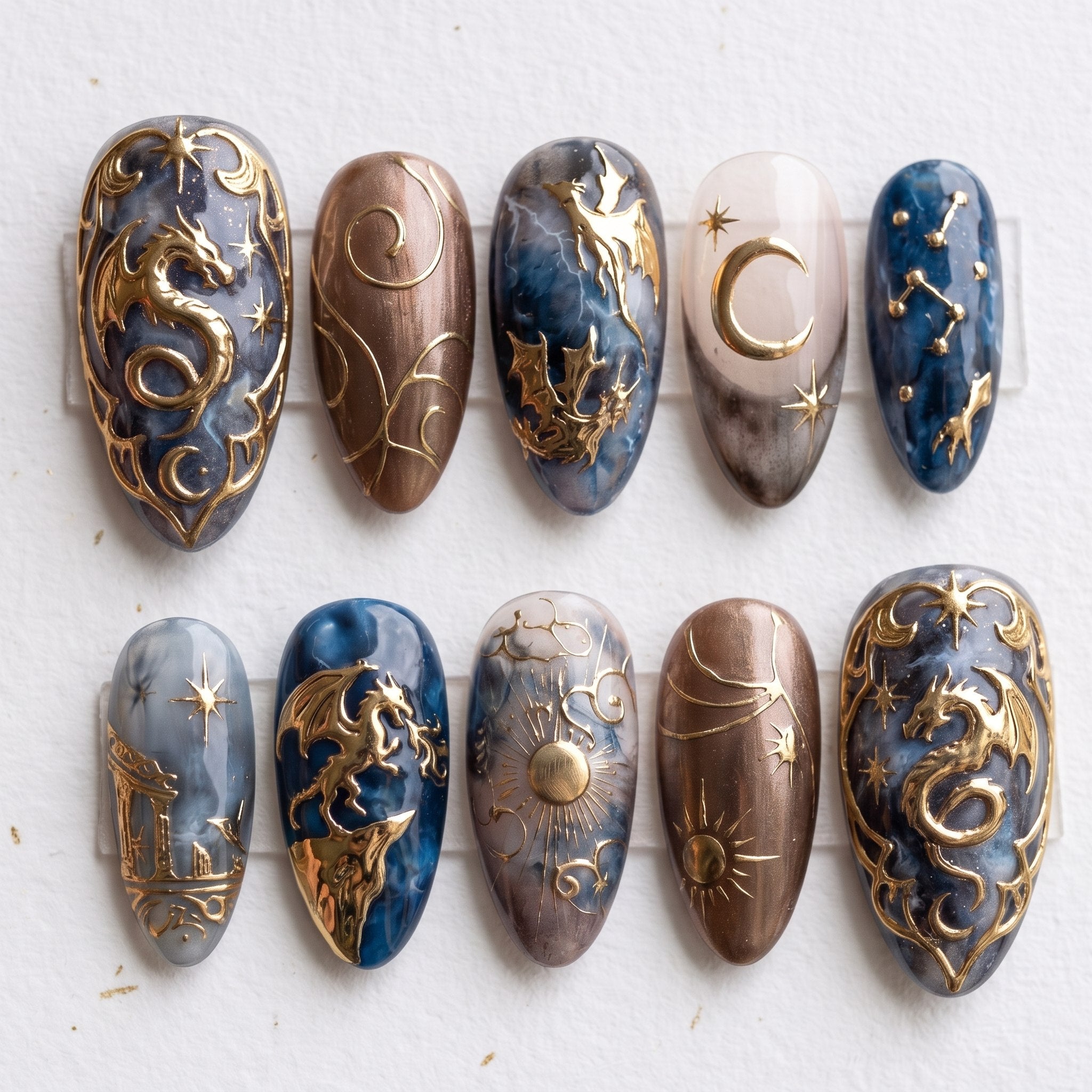 A set of press-on nails featuring detailed metallic gold dragons, celestial sun and moon motifs, and a blue and grey marble design.