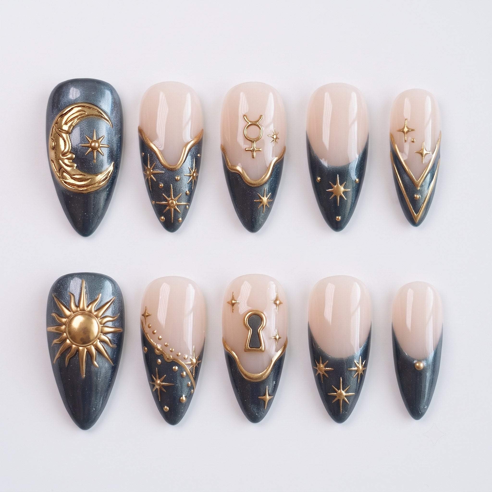 Celestial themed press-on nails in charcoal grey and nude with gold moon, sun, and star embellishments.