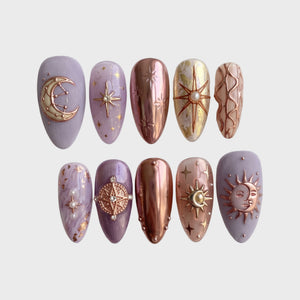 A set of celestial-themed press-on nails featuring lavender matte, rose gold chrome, and 3D star and moon charms.