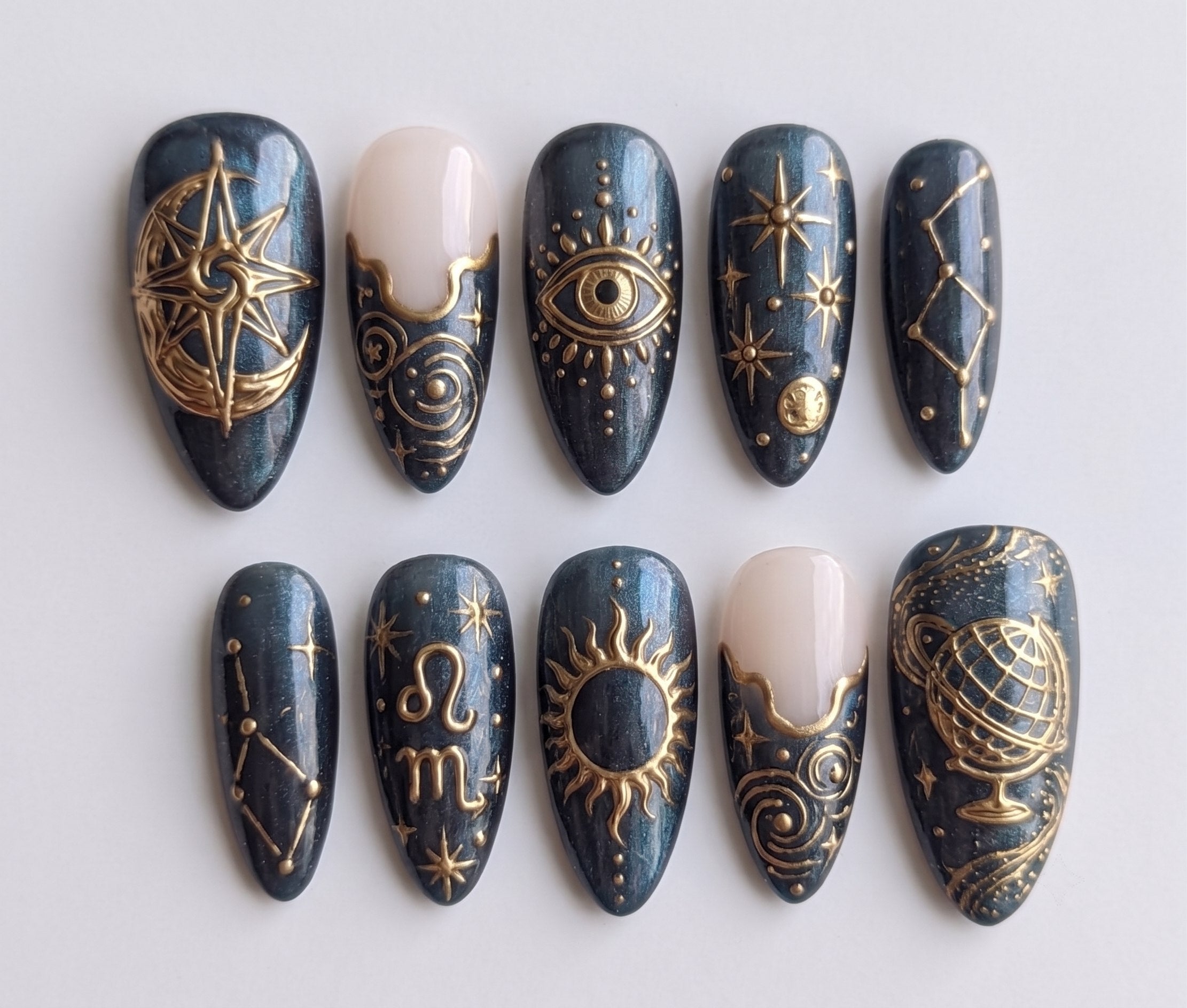 Celestial gold astrology press-on nails featuring sun, moon, and constellation designs on a dark pearlescent base.