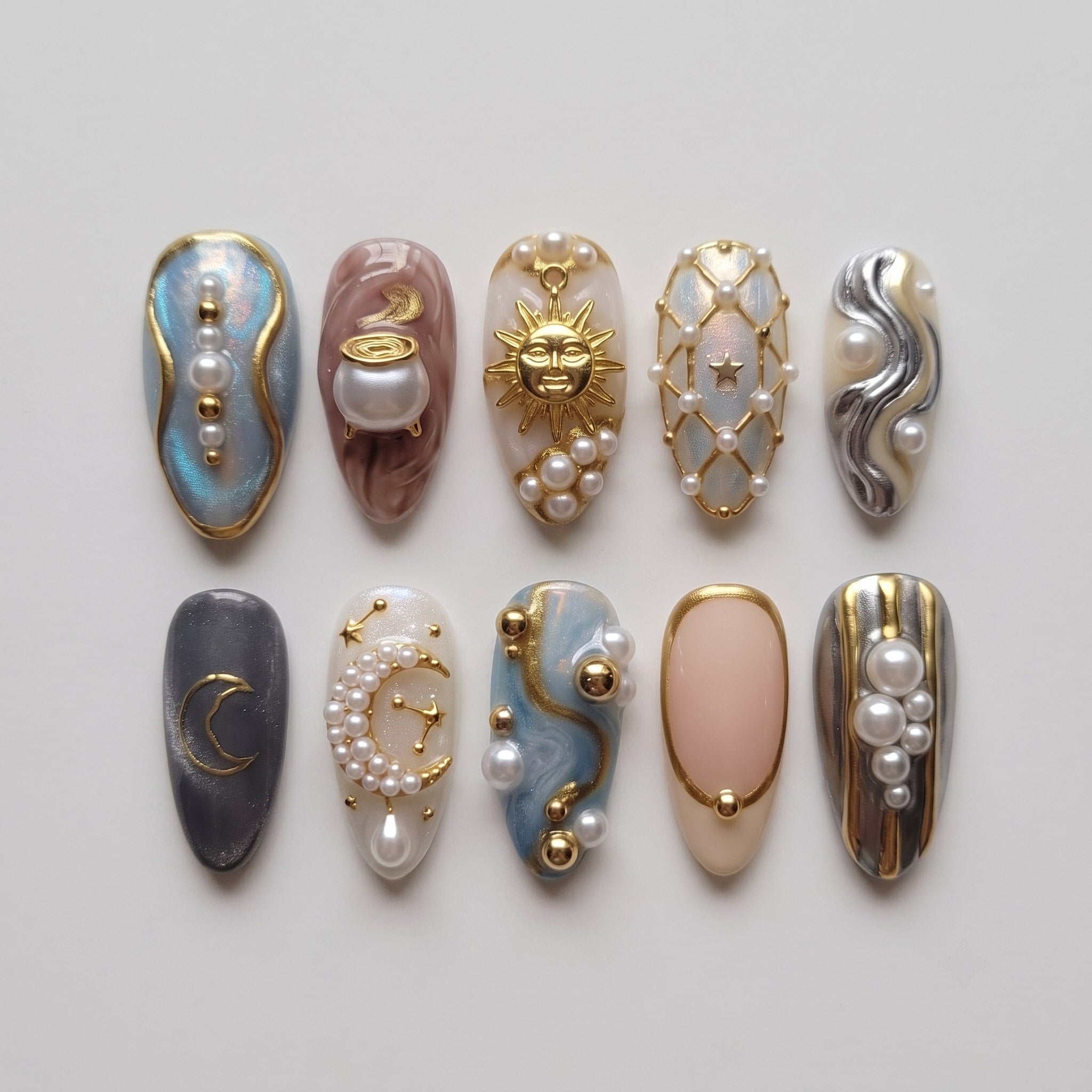 Celestial themed press-on nails featuring gold sun, moon, and cauldron motifs adorned with pearls and gold beads.