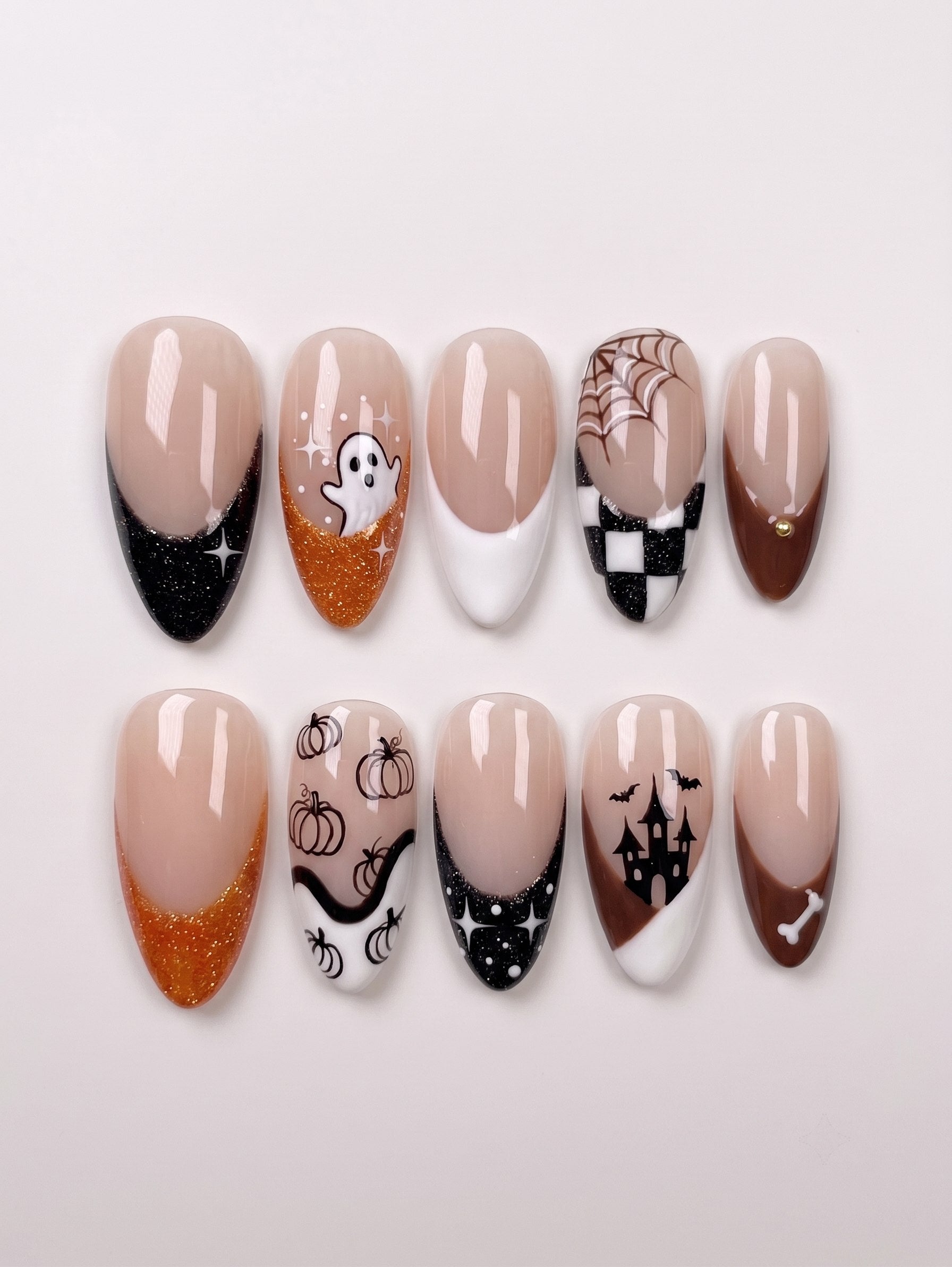A set of ten almond-shaped press-on nails featuring a Halloween theme with ghosts, pumpkins, haunted houses, spiderwebs, and glittery orange and black French tips.