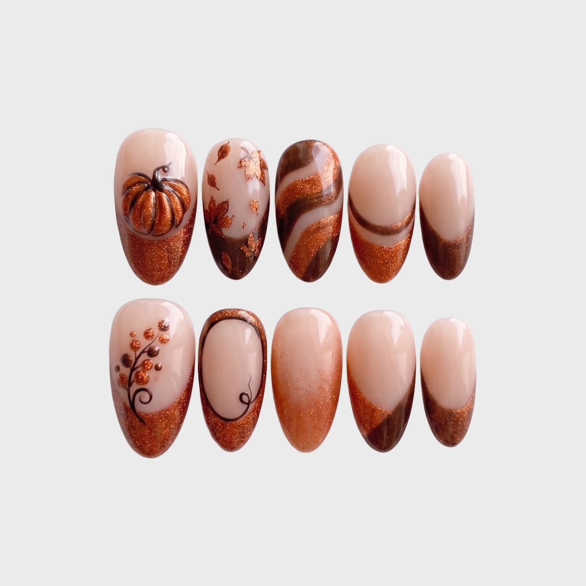 A set of autumn-themed press-on nails featuring copper glitter French tips, a 3D metallic pumpkin, fall leaves, and brown swirl designs on a nude base.