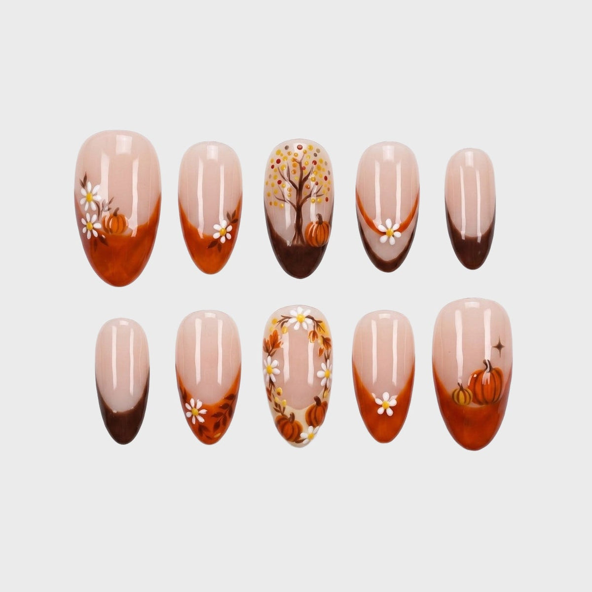 A set of press-on nails featuring a brown and orange French tip design with autumn pumpkins and white daisies.
