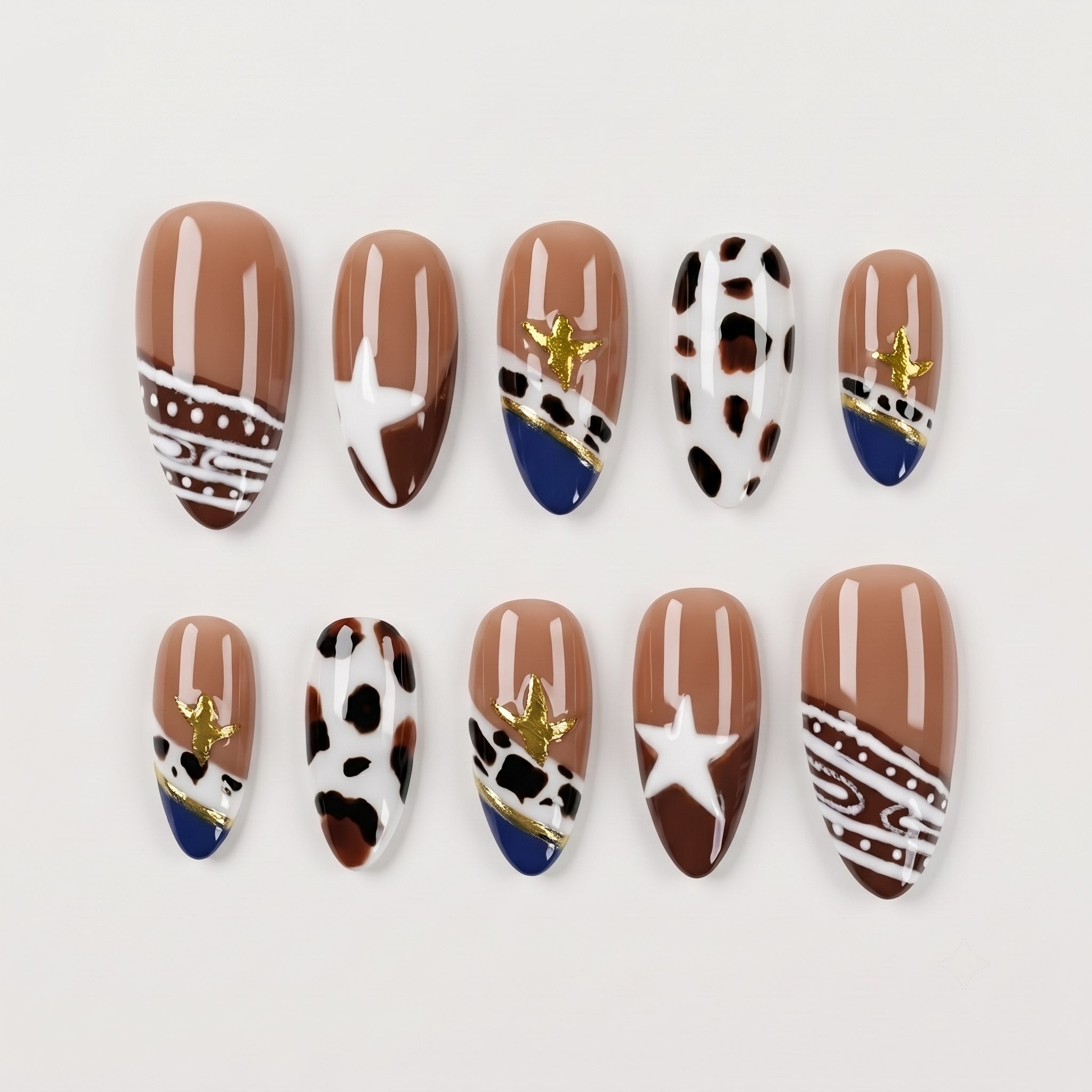 Set of press-on nails with brown, white, and navy patterns, cow print, and gold star details.