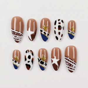 Set of press-on nails with brown, white, and navy patterns, cow print, and gold star details.
