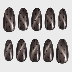 A set of almond-shaped press-on nails featuring a translucent grey cat eye finish and black polka dot pattern.