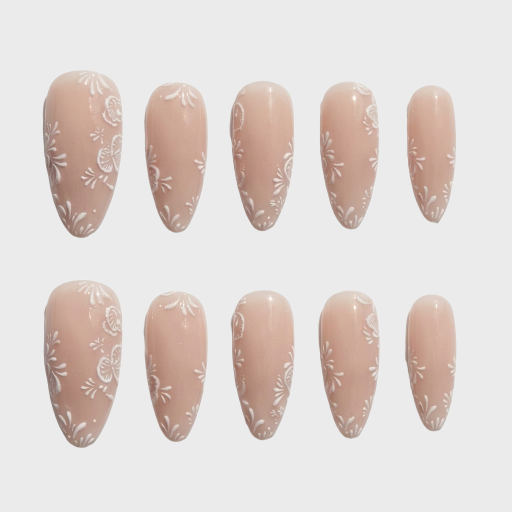 Almond shaped press-on nails in a nude color with white floral line art designs.