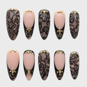 A set of press-on nails featuring black lace patterns, nude French tips, and gold stud embellishments.