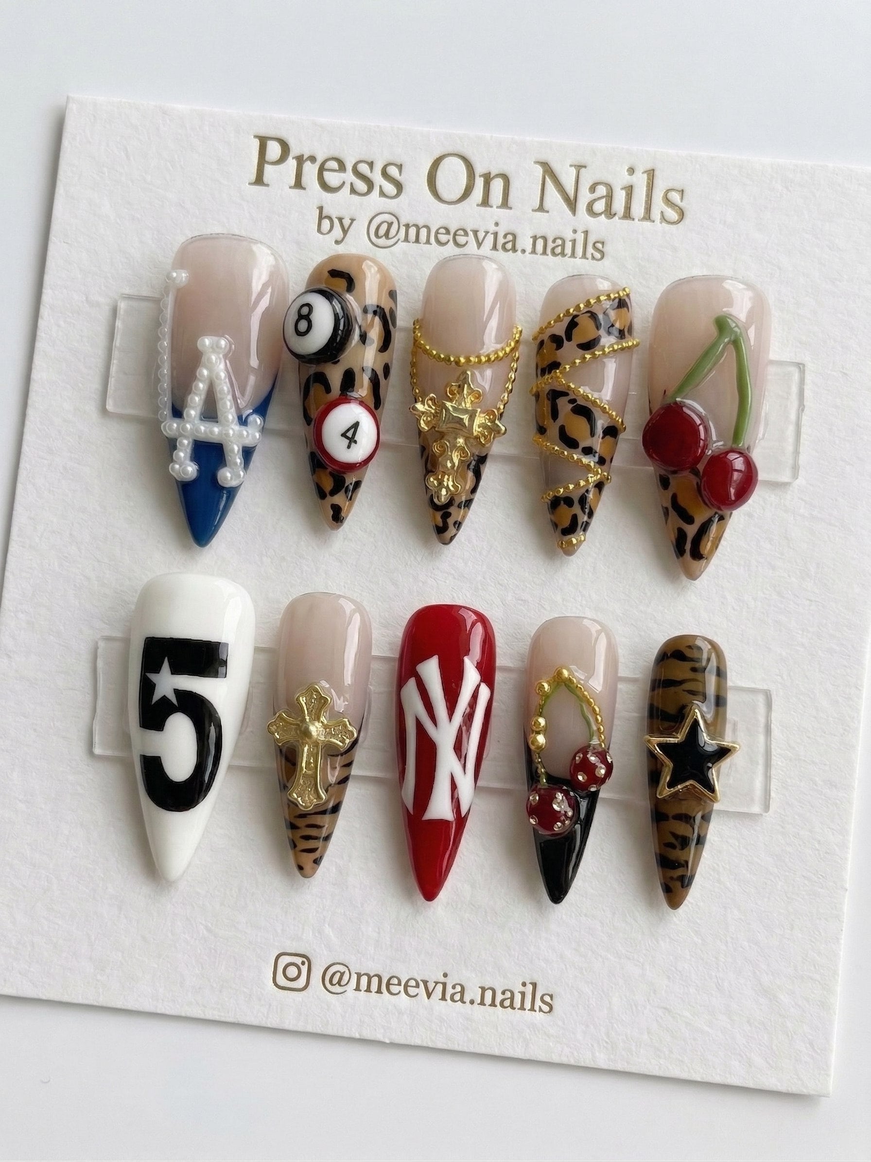 Stiletto-shaped leopard print press-on nails with 3D charms, pool balls, and sports logos.