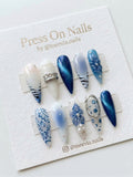 Stiletto-shaped blue and white press on nail set with 3D floral art, lace motifs, and silver accents.