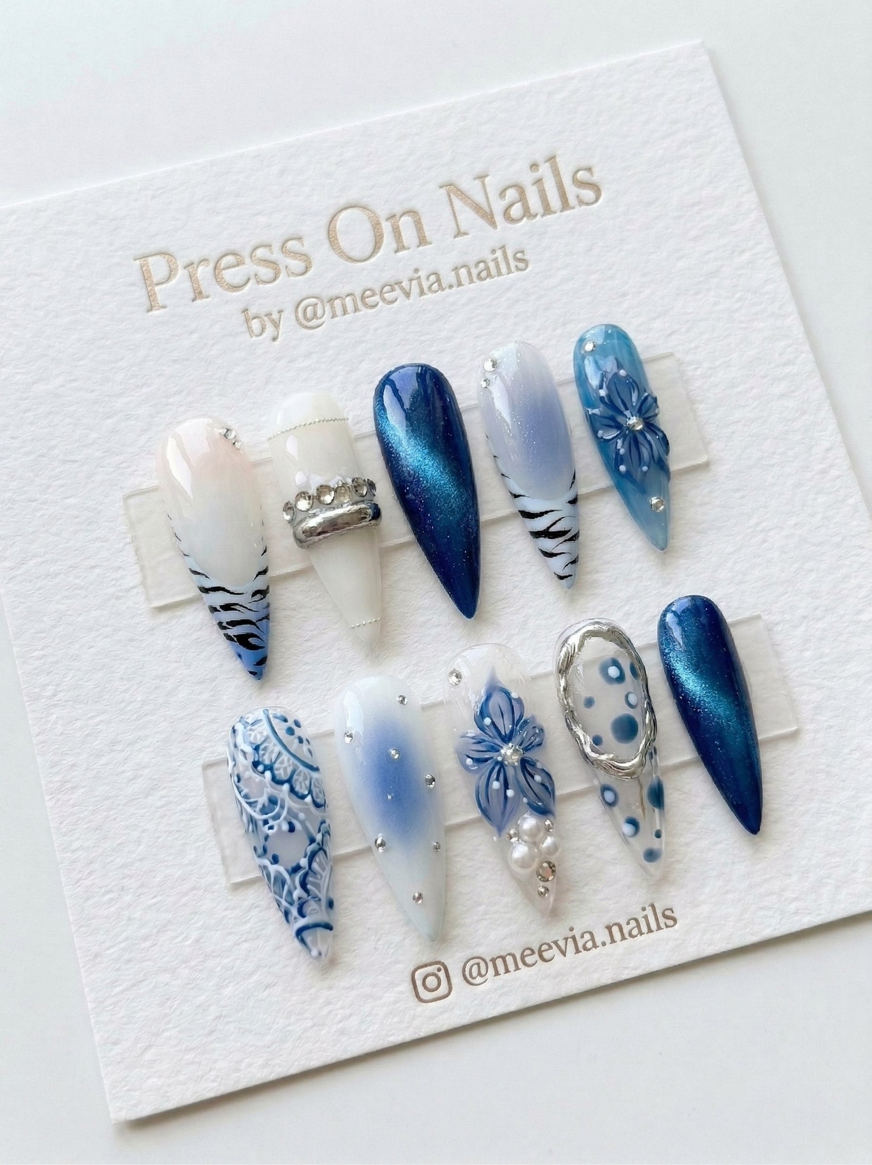 Stiletto-shaped blue and white press on nail set with 3D floral art, lace motifs, and silver accents.