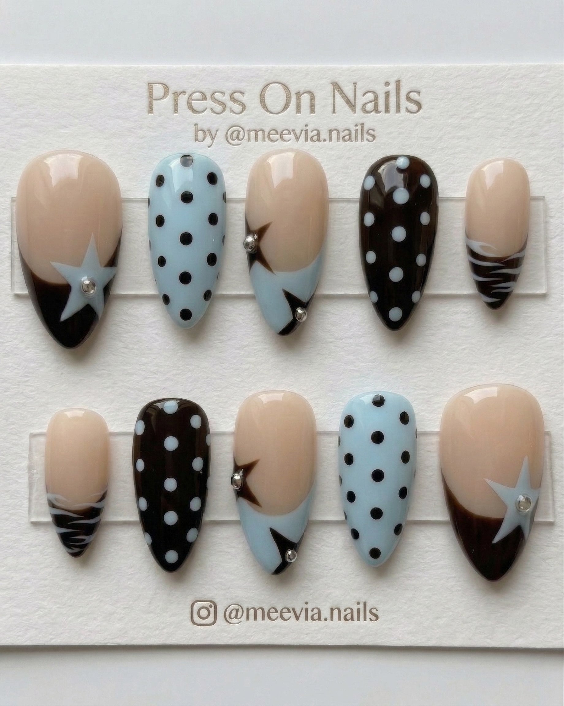 Almond-shaped press-on nail set with brown and blue star motifs, polka dots, and silver studs.