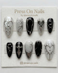 Stiletto-shaped black and white press-on nail set with 3D silver chrome hearts and gothic motifs