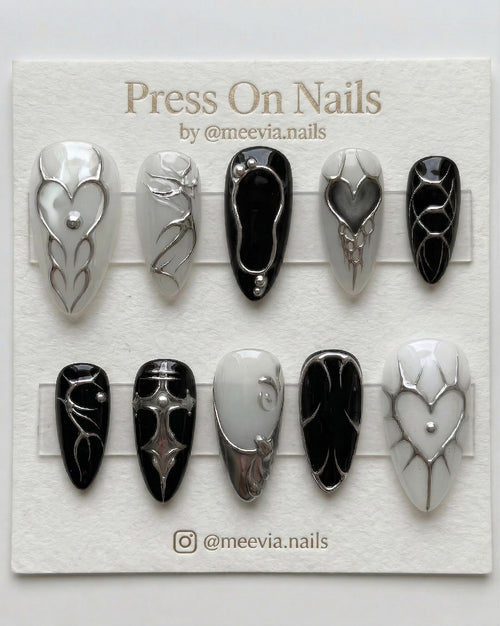 Stiletto-shaped black and white press-on nail set with 3D silver chrome hearts and gothic motifs