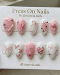 Almond-shaped pink and white press-on nails with 3D bows, hearts, and silver star charms.