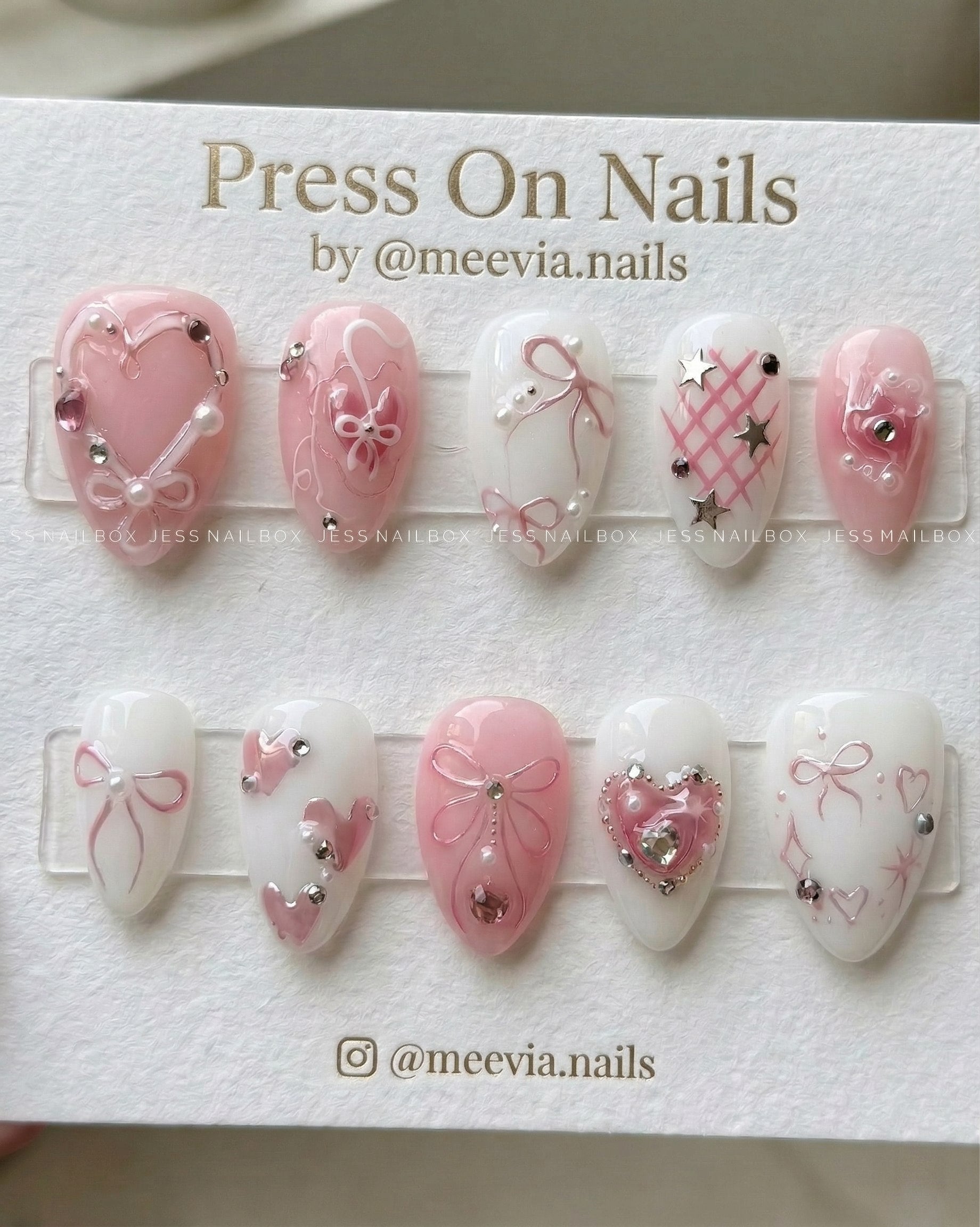 Almond-shaped pink and white press-on nails with 3D bows, hearts, and silver star charms.