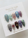 Long almond-shaped press-on nails with mixed designs including 3D hearts, butterflies, and iridescent finishes.