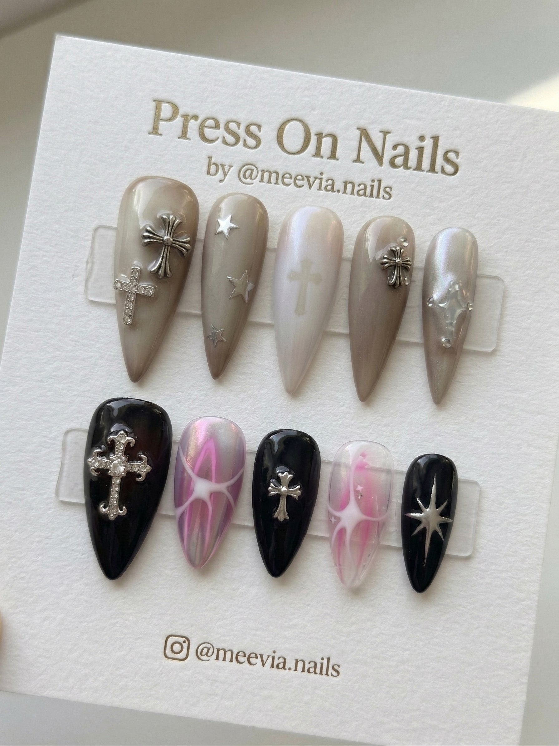 Stiletto-shaped gothic press-on nail set featuring silver cross and star charms in black and taupe colors.