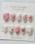 Almond-shaped pink and white coquette press on nails with 3D bows, hearts, and silver stars.