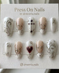 Almond-shaped white glazed press-on nail set with silver 3D scrolls, a red heart, and a dark cross.