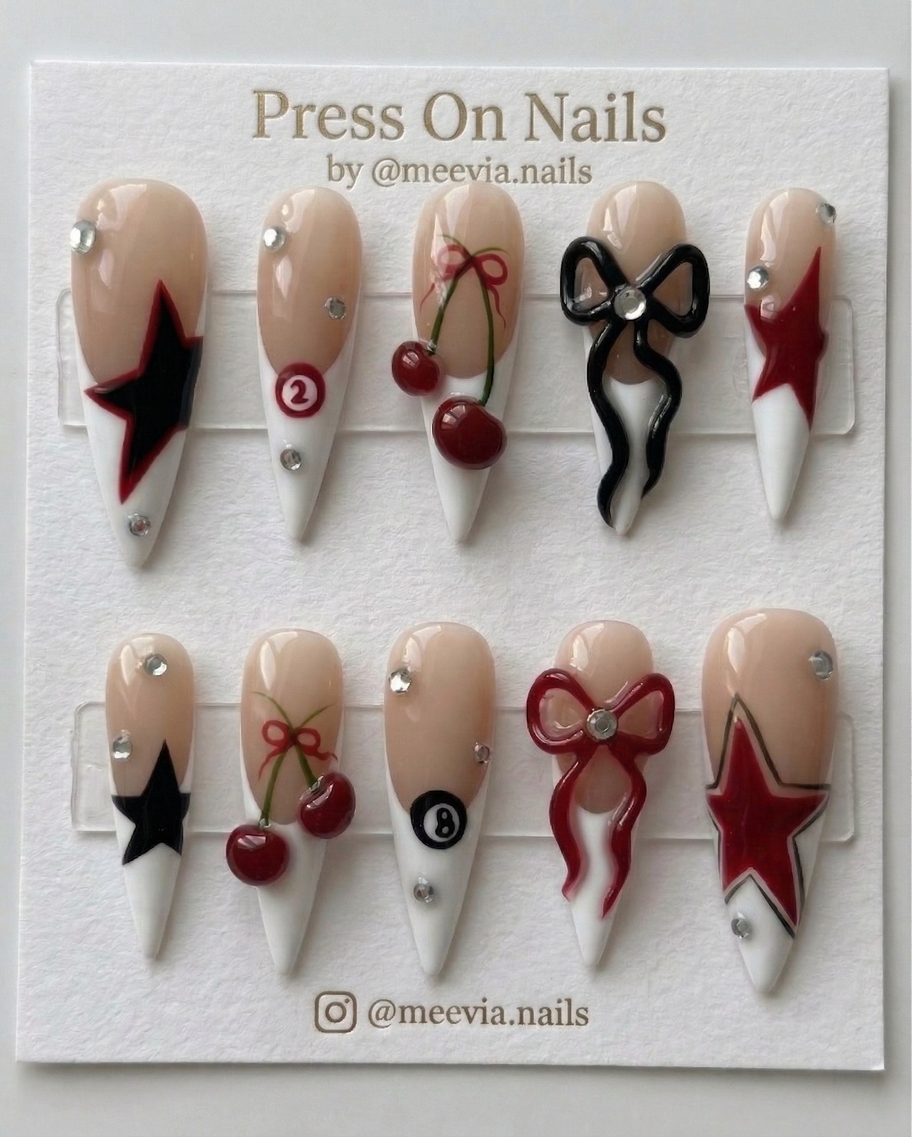 Long stiletto press on nails featuring 3D red and black bows, cherries, stars, and billiard ball designs.