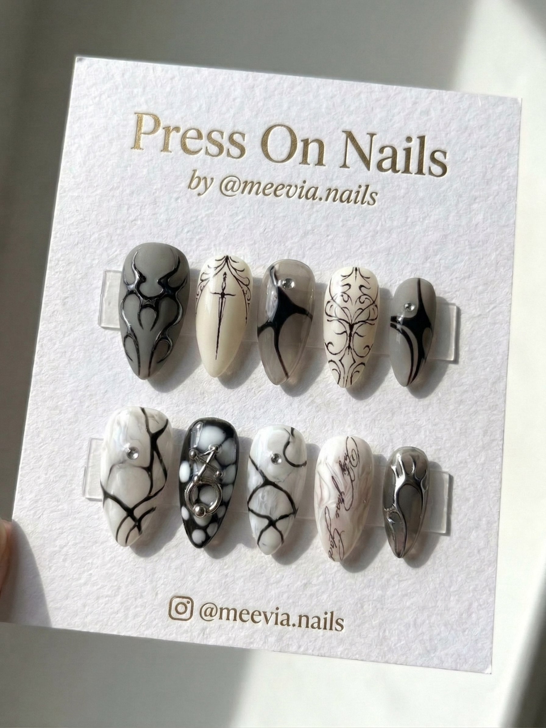 Almond-shaped grey and black press-on nails with cyber sigilism patterns and 3D metallic accents.