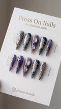 Stiletto-shaped purple galaxy press-on nails with silver 3D metallic swirls and clear jelly droplets