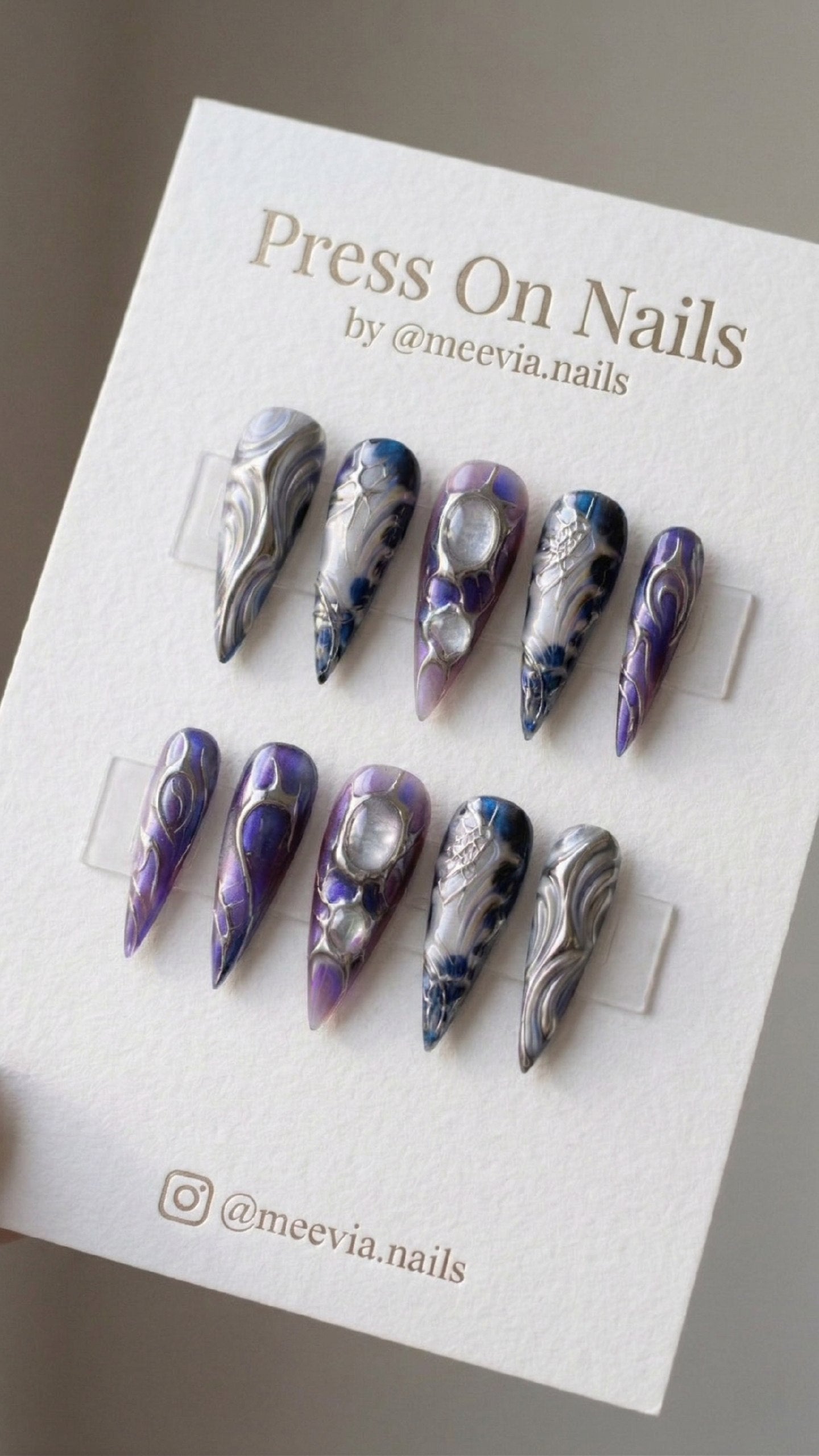 Stiletto-shaped purple galaxy press-on nails with silver 3D metallic swirls and clear jelly droplets