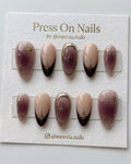 Almond-shaped plum and nude press-on nail set with gold celestial star motifs and metallic gold frames.
