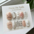 Short oval press-on nail set featuring 3D cats, paw prints, and pearl embellishments on nude and clear bases.