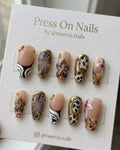 Long coffin-shaped press-on nails with safari animal prints, 3D brown flowers, and gold chrome detailing.