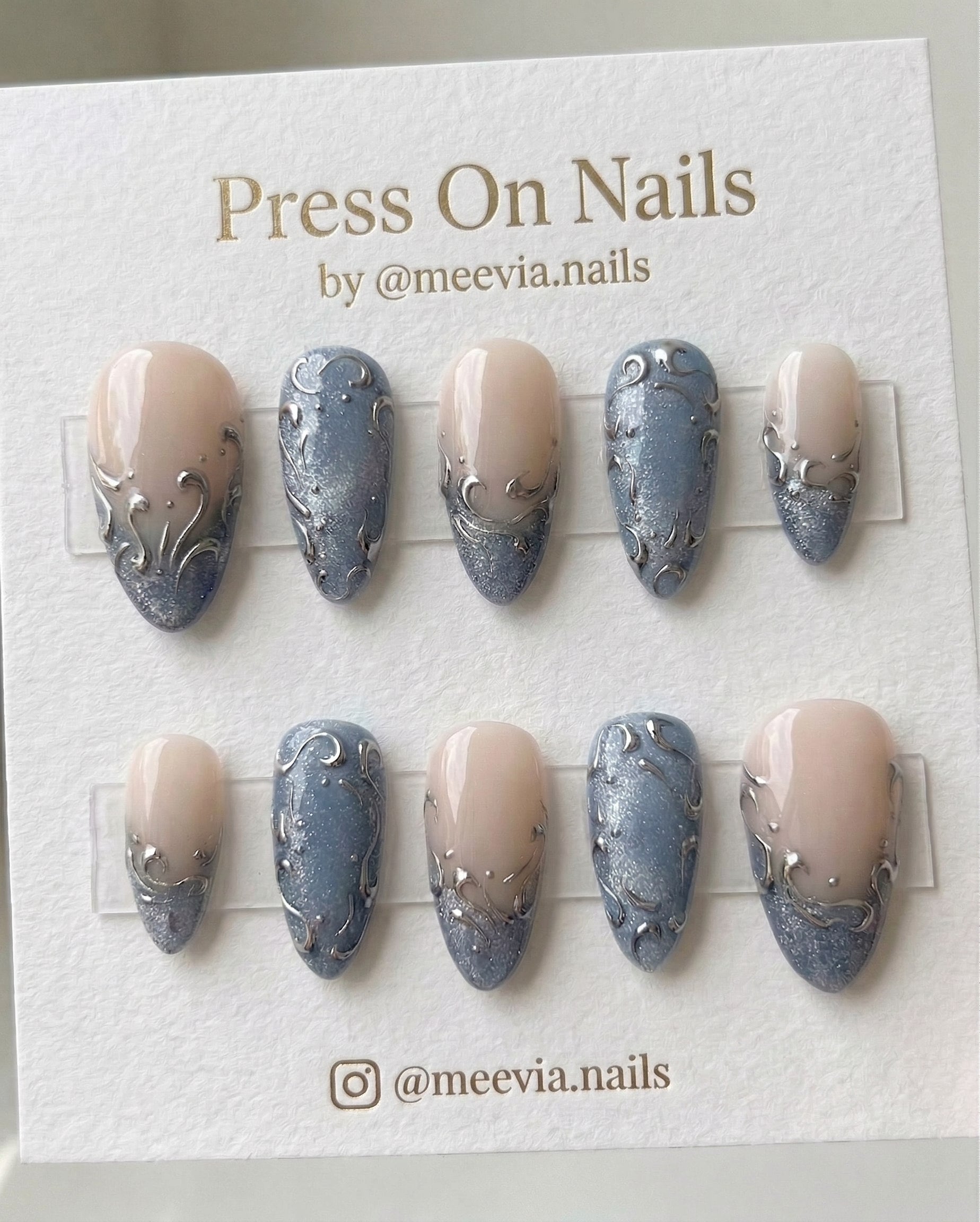 Almond-shaped blue glitter press-on nail set with silver 3D swirl art and nude ombre finish
