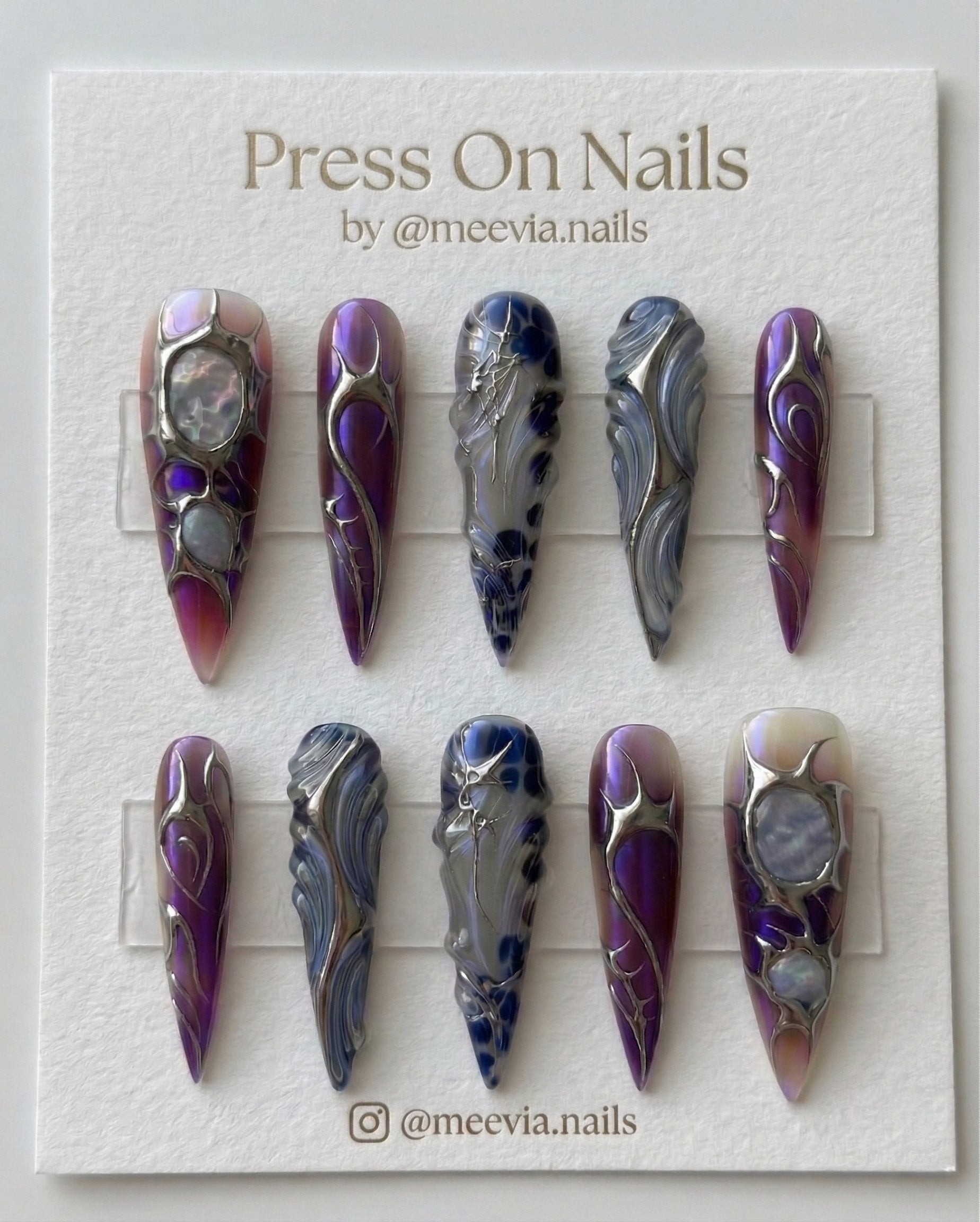 Long stiletto press on nails featuring purple chrome, 3D silver metallic swirls, and iridescent blue marble details.