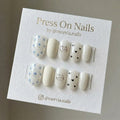 Oval white press-on nail set with blue floral patterns, a cute cat face, and black hearts