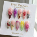 Stiletto-shaped press-on nails with 3D flowers, animal prints, and jelly droplets in a colorful artistic nail set.