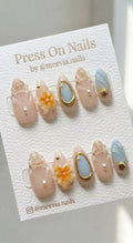 Almond-shaped press on nails featuring 3D seashell art, orange flowers, and gold sea charms.