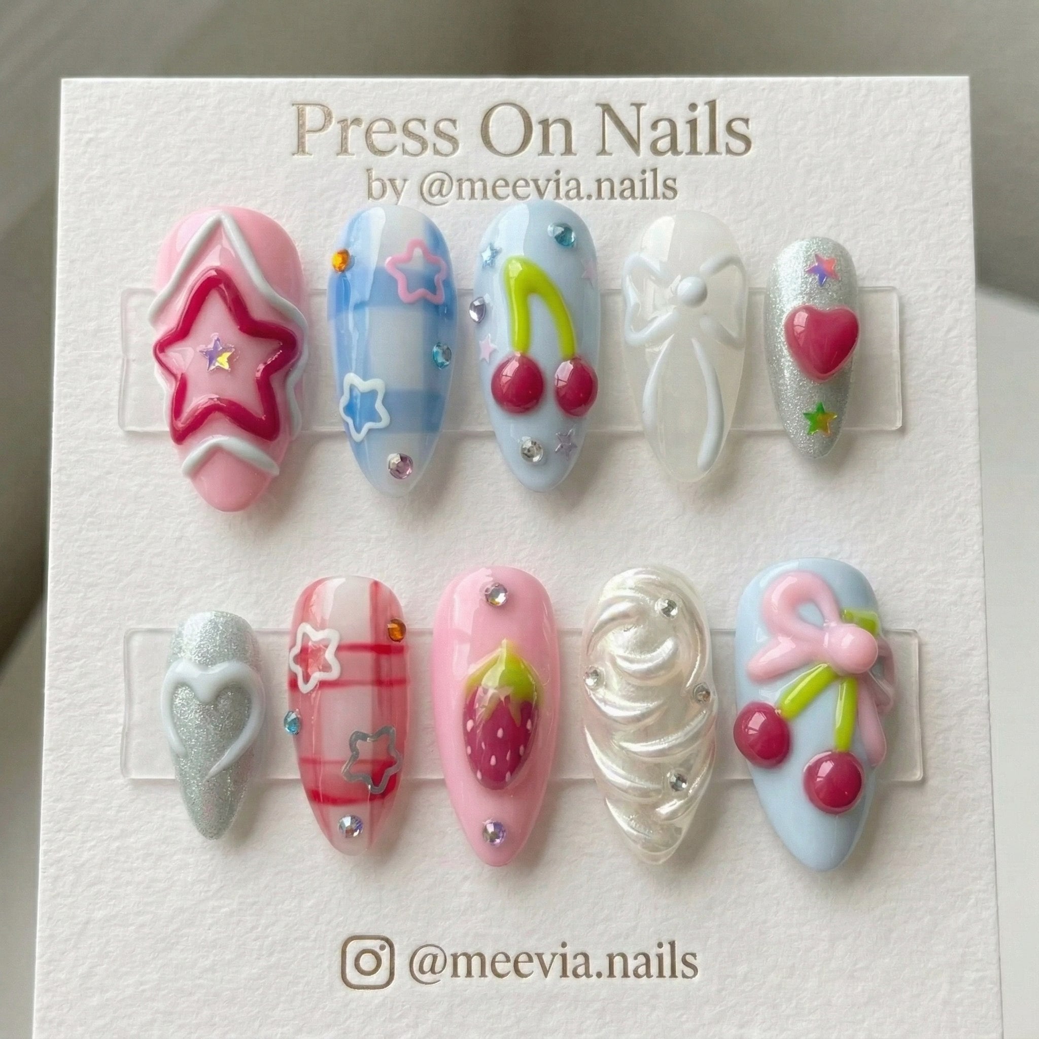 Almond-shaped press on nails with 3D cherry, star, and bow motifs in pink and blue