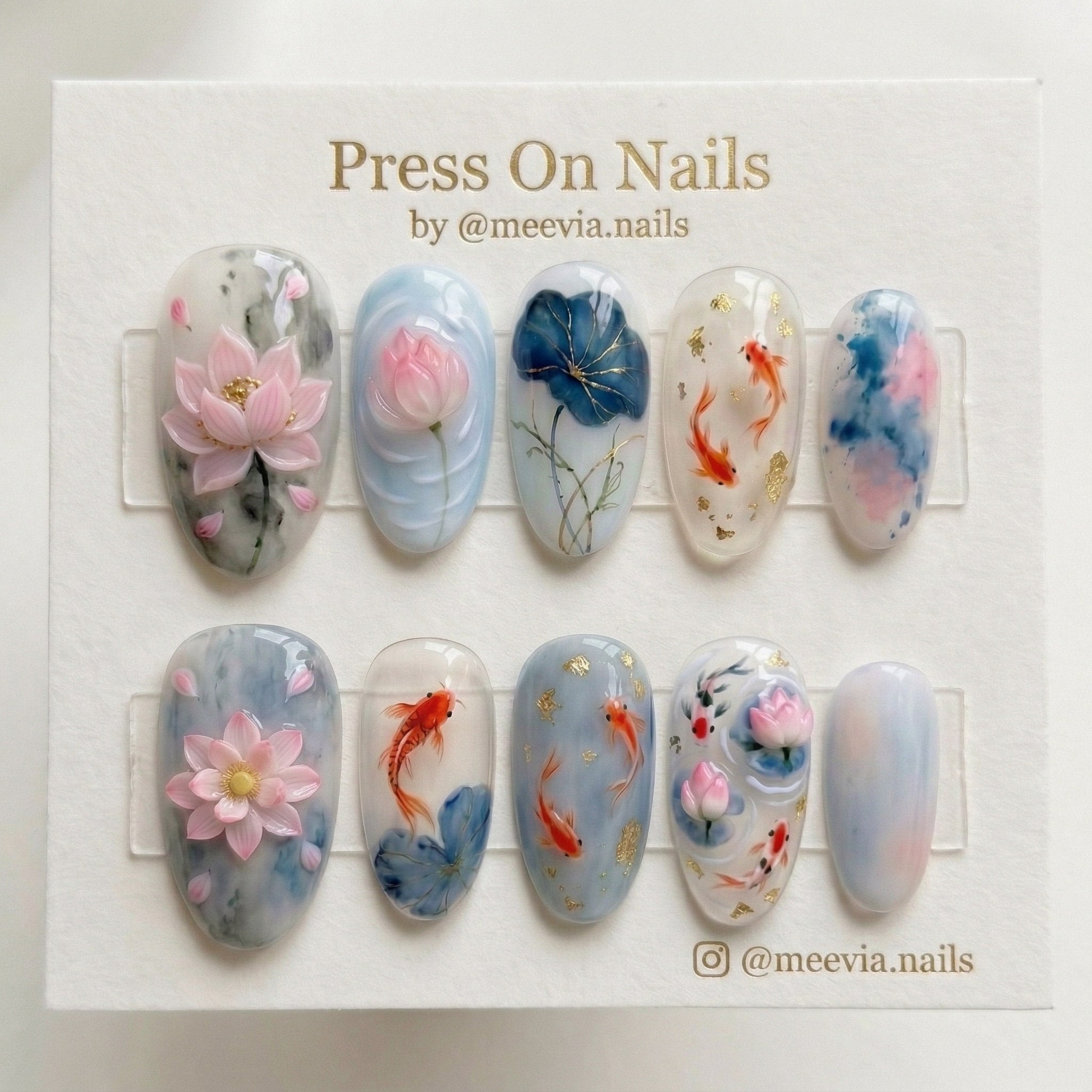 Oval-shaped press-on nails featuring 3D pink lotus flowers, orange koi fish, and gold flakes on a blue watercolor base.