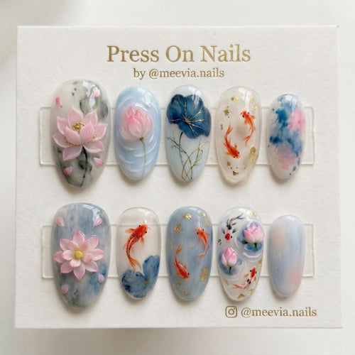 Oval-shaped press-on nails featuring 3D pink lotus flowers, orange koi fish, and gold flakes on a blue watercolor base.
