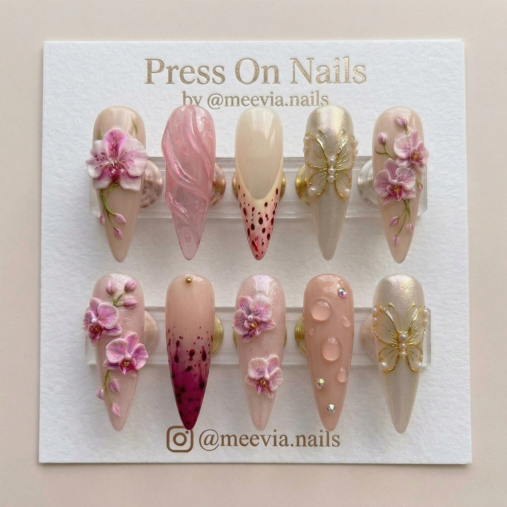 Stiletto-shaped press-on nails with 3D pink orchids, gold butterfly charms, and magenta splatter nail art