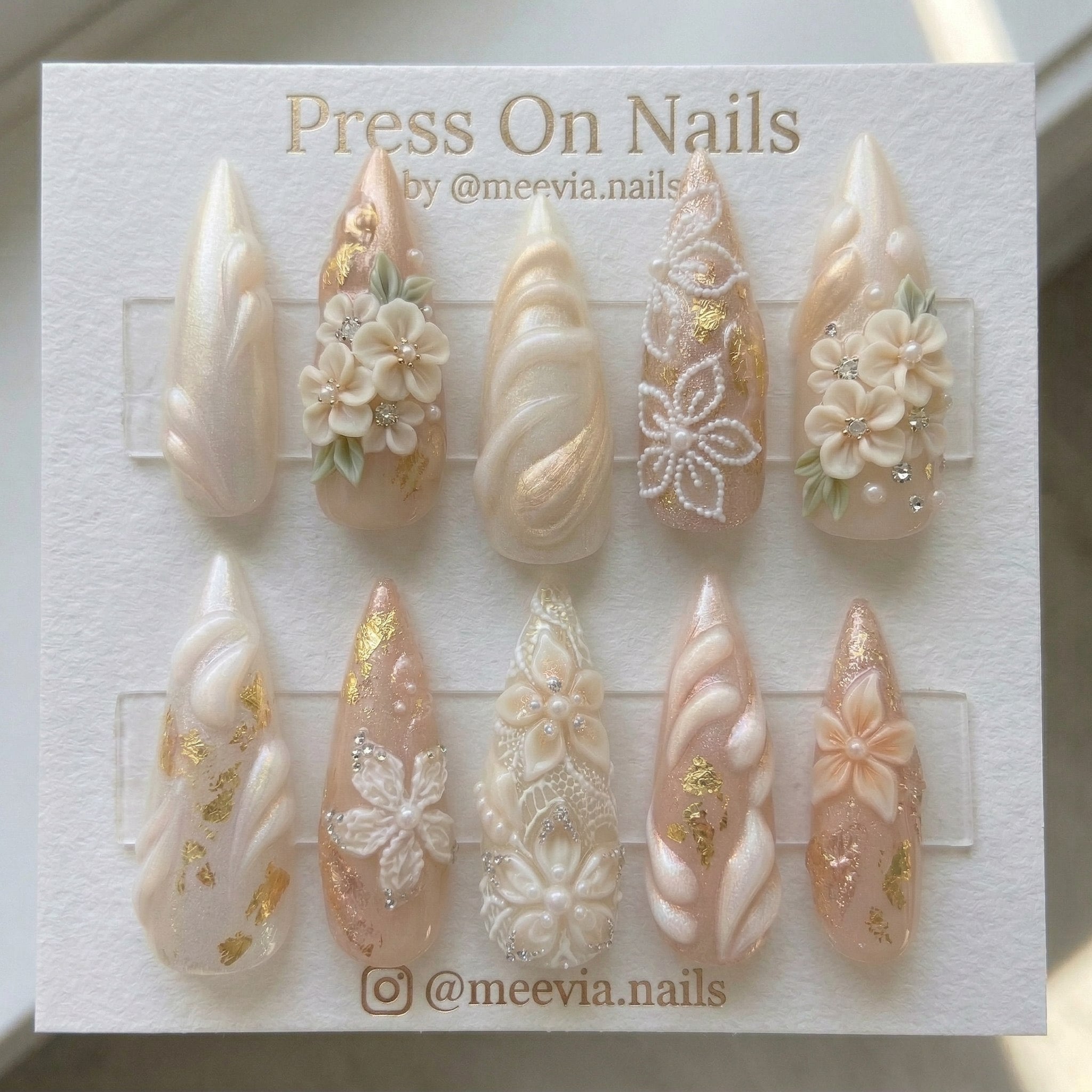 Stiletto-shaped pearl shimmer press-on nail set with 3D floral art and gold foil accents