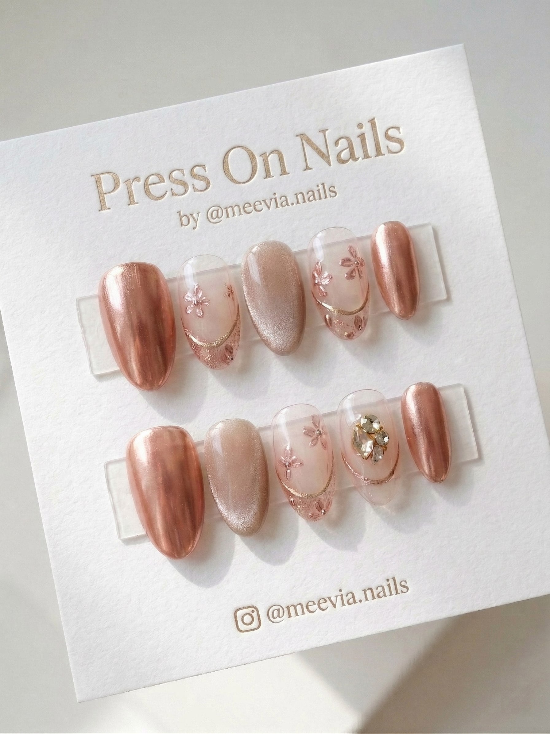 Almond-shaped rose gold chrome press-on nails with 3D floral art and rhinestone embellishments