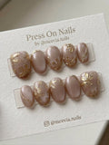 Oval-shaped taupe shimmer press-on nail set with 3D gold floral motifs and metallic accents