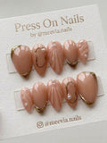 Almond-shaped nude press-on nail set with 3D shell textures and gold metallic accents