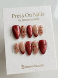 Almond-shaped press-on nail set featuring red shimmer finish and hand-painted cherry motifs on a nude base.