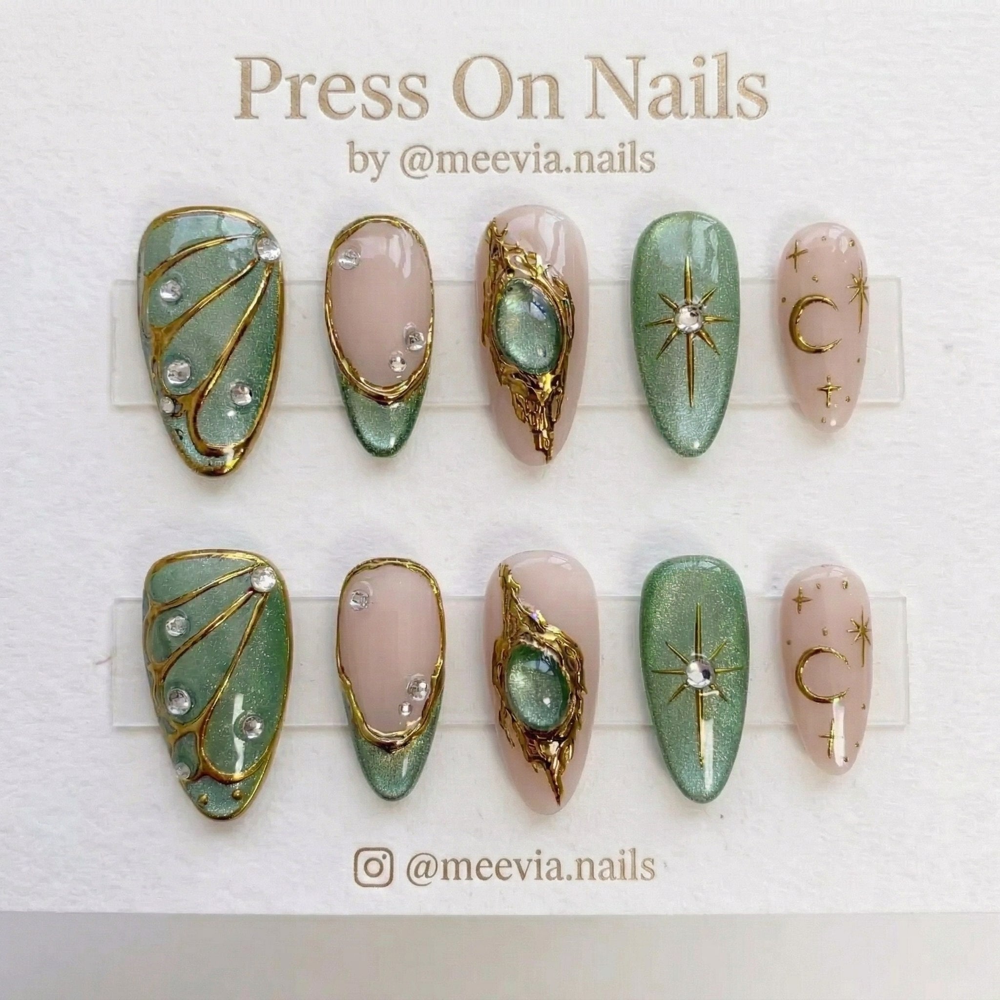 Almond-shaped sage green and nude celestial press-on nails with gold 3D art and star motifs.