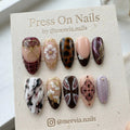 Almond-shaped press-on nails with 3D floral art, tortoiseshell print, and burgundy marble designs.