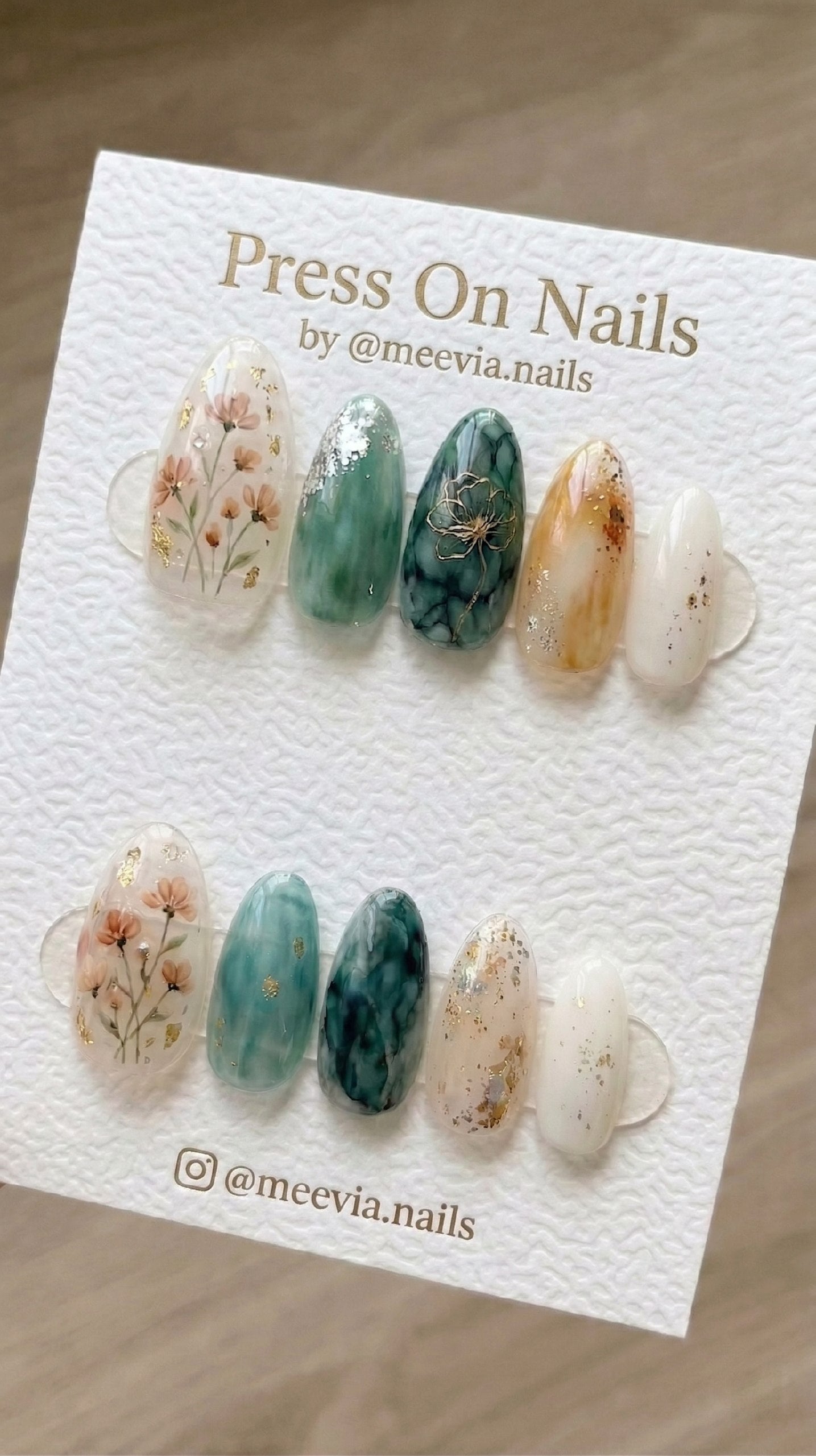Almond-shaped press-on nails featuring floral art and teal marble designs with gold foil accents.