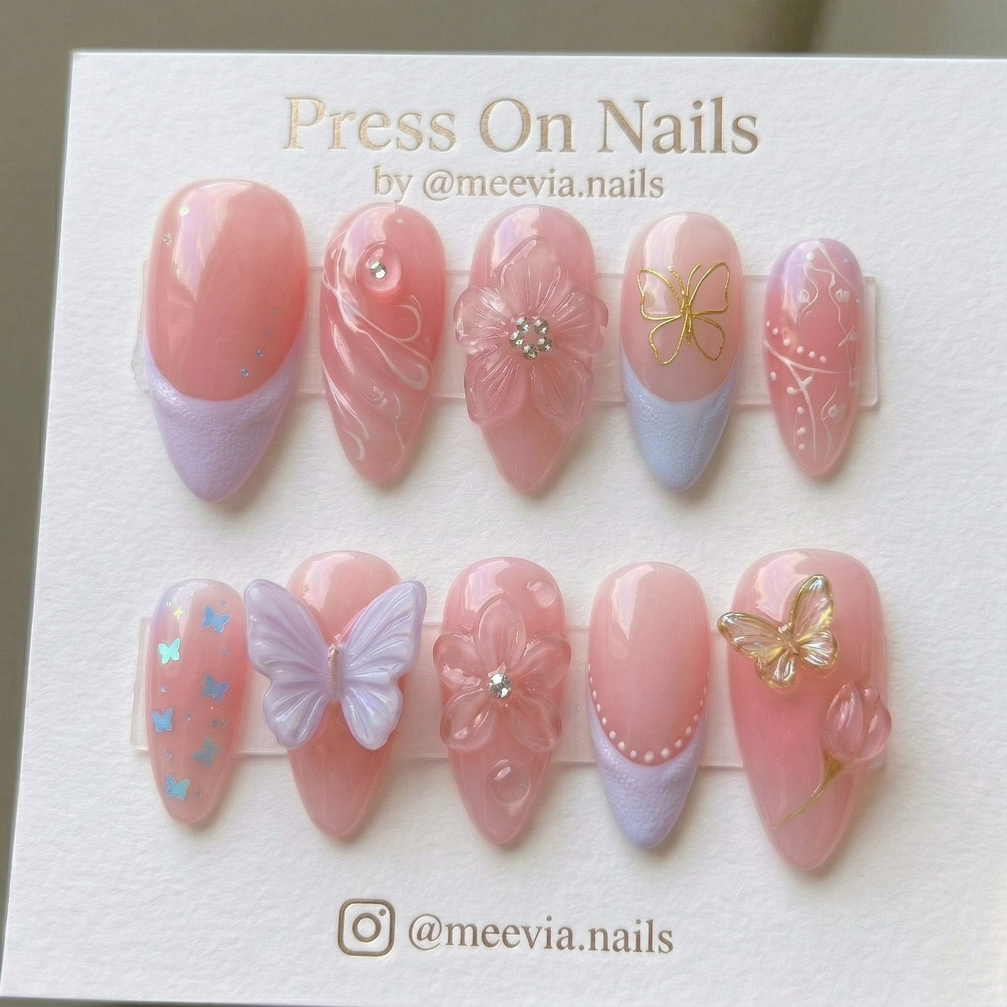 Almond-shaped pink press-on nails with 3D butterflies, floral art, and lavender French tips